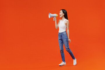 Fototapeta na wymiar Full size side view vivid young woman of Asian ethnicity 20s years old in white tank top hold scream in megaphone announces discounts sale Hurry up isolated on plain orange background studio portrait.