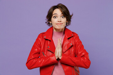 Young smiling happy woman 20s in red leather jacket hold hands folded in prayer gesture, beg about...