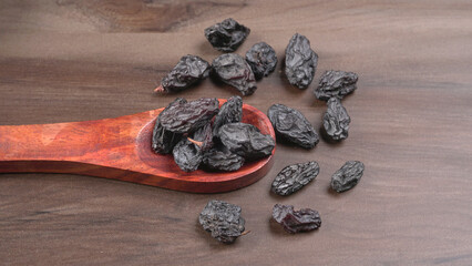 black raisins in a bowl on a wooden table. black raisins in a spoon