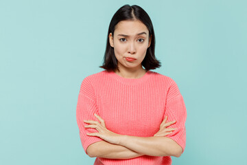 Young sad offended shrewd woman of Asian ethnicity 20s wearing pink sweater hold hands crossed folded isolated on pastel plain light blue color background studio portrait. People lifestyle concept