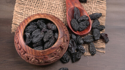 black raisins in a bowl on a wooden table. black raisins in a spoon