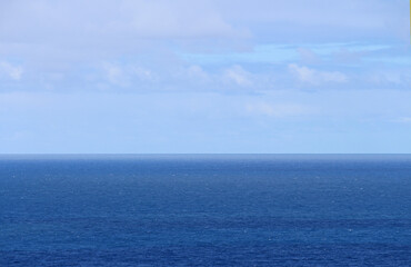 Flat blue ocean, straight horizon, blue sky and soft clouds. Sydney Australia