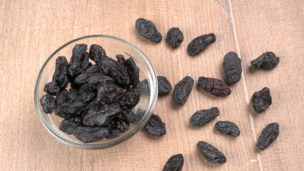 black raisins in a bowl on a wooden table. black raisins in a spoon