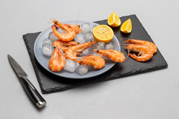 Shrimps, lemon and ice on a gray plate and on a stone surface.