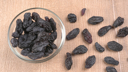 black raisins in a bowl on a wooden table. black raisins in a spoon