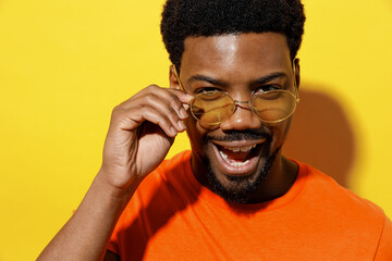 Close up young cool man of African American ethnicity 20s in basic casual orange t-shirt take off glasses listen music in earphones isolated on plain yellow background studio People lifestyle concept