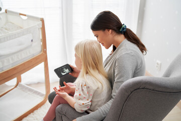 Caucasian woman in advanced pregnancy and her elementary aged daughter using mobile phone at home