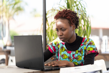 Serious young african girl sitting at her laptop and looking for a job on the internet; social...
