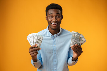 Excited black guy holding stack of Dollars in yellow studio