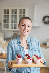 Young baker woman holding cupcakes. Happy, smiling and cheerful. Modern kitchen.