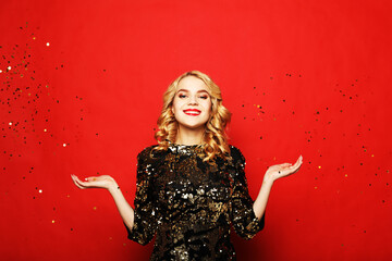 Holiday and party concept: beautiful young woman wearing evening dress standing under confetti rain...