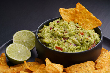 Guacamole dip with tortilla chips or nachos and lime on a black background