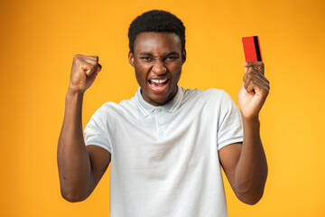 Afro american man holding red credit card against yellow background in studio