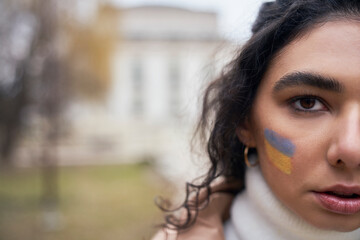 Close up half face of young woman with Ukrainian flag painted on her cheek