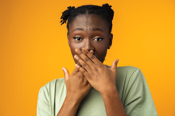 Young black woman covering mouth with hands against yellow background