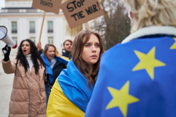 Man and woman covered with EU and Ukraine flags standing face to face and talking.