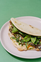 Italian Piadina with oyster mushrooms, spinach, pesto, mozzarella, bechamel, gorgonzola cheese, green onions. Green background. Close up