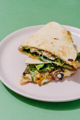 Italian Piadina with oyster mushrooms, spinach, pesto, mozzarella, bechamel, gorgonzola cheese, green onions. Green background. Close up
