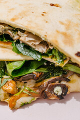 Italian Piadina with oyster mushrooms, spinach, pesto, mozzarella, bechamel, gorgonzola cheese, green onions. Green background. Close up