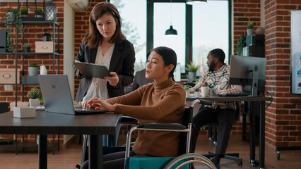 Asian woman in wheelchair brainstorming ideas with colleague, doing teamwork to plan business...