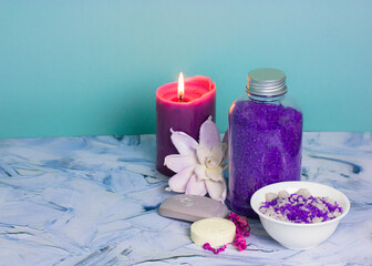 Fototapeta na wymiar Composition with a jar of purple lavender sea salt, soap bar, burning lilac candle and beautiful flower. Spa procedure, body, facial care. Cosmetic products. Bathing treatments in a beauty salon.