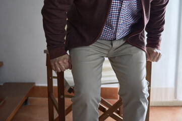 A mature man has difficulty getting up from an armchair in the living room of his home.