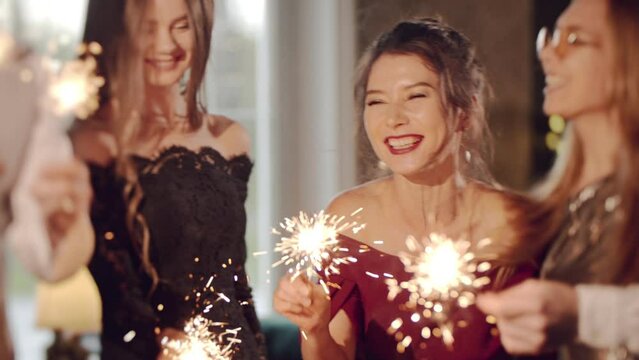 Asian girl and group young college student friends lit light sparkler in hand fireworks, sing and dance together. Woman on Party with people, love friendship relationship and celebration concept.