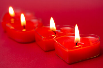 Four red burning heart-shaped candles with blazing flames. Tongues of fire on a red background. Valentine's Day, passion, love, feelings concept. Monochrome wallpaper. I love you decor for February 14
