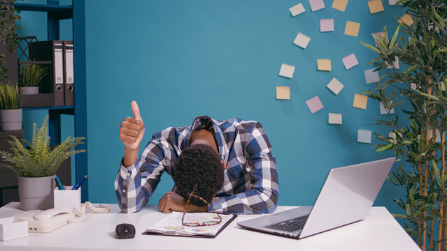 Tired Employee Resting Head On Desk And Giving Thumbs Up In Front Of Camera, Feeling Sleepy At Office Job. Exhausted Overworked Man Showing Okay And Approval Symbol. Ok Gesture