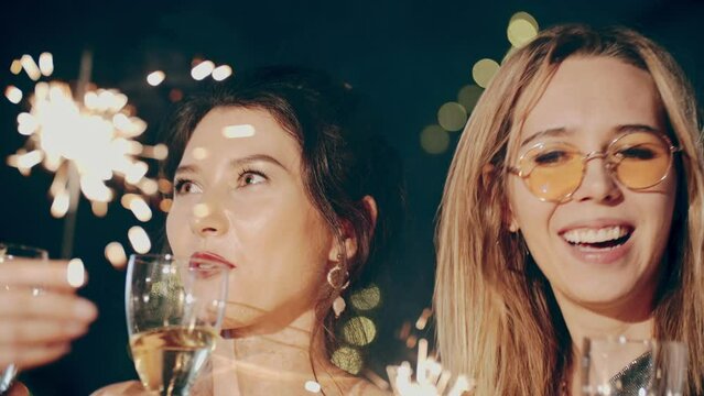 Close up portrait of friends at party celebrating birthday, drinking champagne or sparkling wine, pouring into glass, smiling, laughing, holding and waving sparkler. Happiness or fun concept.