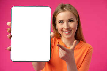 Young smiling woman showing digital tablet with blank screen against pink background