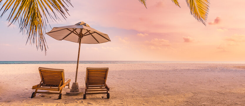 Beautiful panoramic nature. Tropical beach sunset as summer island landscape with chairs umbrella palm leaves calm sea shore, coast. Luxury travel panoramic destination banner for vacation or holiday © icemanphotos