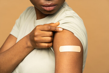 African american woman with adhesive plaster on shoulder after getting coronavirus vaccine isolated on beige wall. Vaccinated black girl and covid-19 vaccination injection. Immunization and health