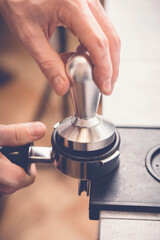Obraz premium Barista tampering coffee in portafilter using tamper. Close-up fresh coffee preparation process