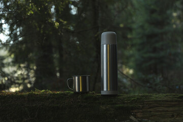 Thermos and cup on log in forest