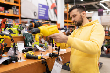a man chooses a new drill for household needs in a power tool store