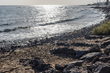 Fototapeta premium Volcanic beach with dark sand and rocks and a shelter against the wind in Playa de Matagorda, Lanzarote, Canary Islands, Spain