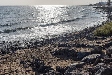 Volcanic beach with dark sand and rocks and a shelter against the wind in Playa de Matagorda, Lanzarote, Canary Islands, Spain