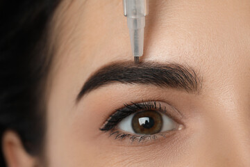 Young woman undergoing procedure of permanent eyebrow makeup in salon, closeup