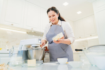 A women cook adds a butter to prepare dough or cream in a mixer bowl.