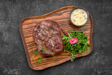 Grilled steak with sauce and herbs, on a wooden board