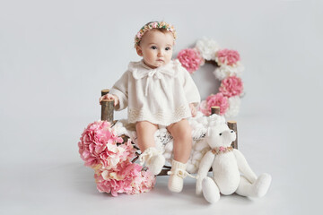 Cute baby girl in knitted clothes and wreath with teddy bear toy. Spring background with flowers. Children Protection Day. Mother's day greeting card. International day of happiness