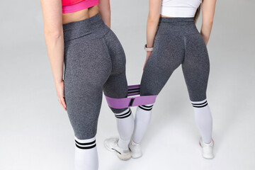 Two women in beautiful fitness leggings with attractive buttocks and a fitness elastic band pose in...