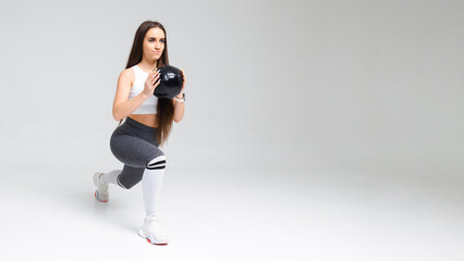 Young athletic woman doing lunges holding a medicine ball in her hands. .Studio shot of sports girl on white background