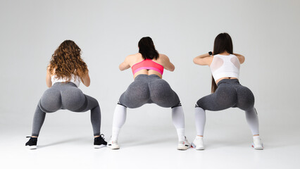 Three young fitness women squat in the studio. Girls with beautiful buttocks are doing a warm-up