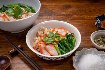 Red Pork Wonton Noodles in hot soup and vegetable. Wonton Noodles in white bowl on wooden background.