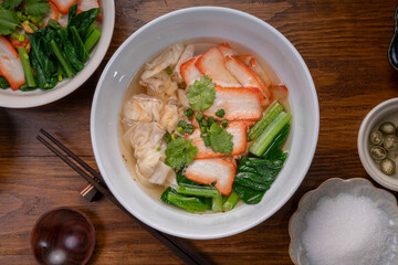 Red Pork Wonton Noodles in hot soup and vegetable. Wonton Noodles in white bowl on wooden background.