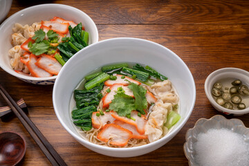 Red Pork Wonton Noodles in hot soup and vegetable. Wonton Noodles in white bowl on wooden background.