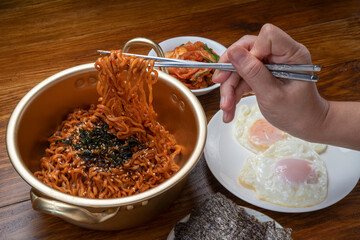 Hand using chopsticks to pick up  Ramyeon noodle in a traditional korean noodle pot, Spicy Korean...