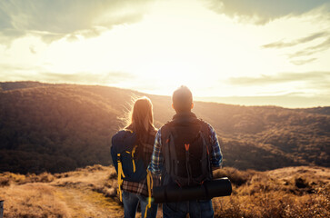 Rear view of couple with backpacks hiking together in nature on autumn day.